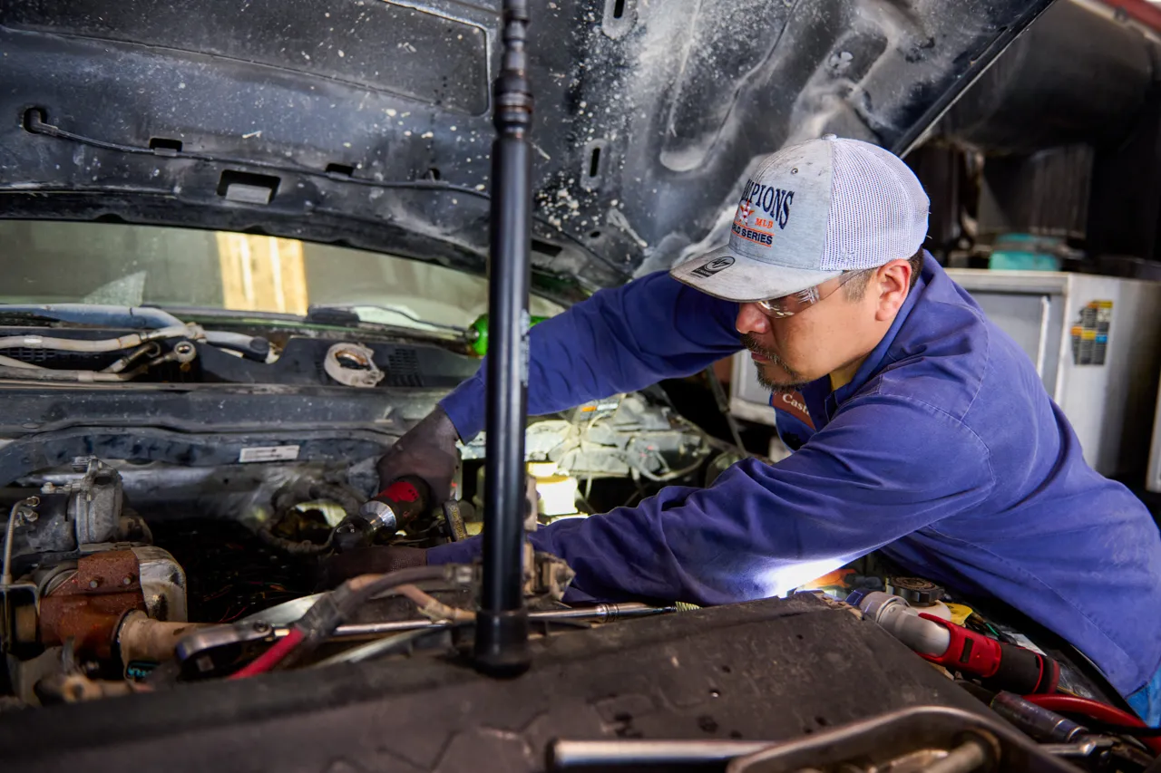 Mechanic inspecting truck suspension components under a lifted heavy-duty truck.